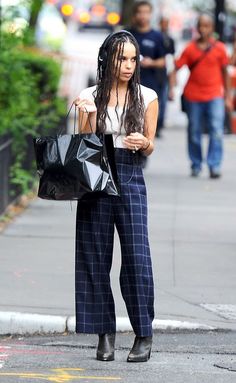 a woman with dreadlocks is walking down the street holding shopping bags and looking at her cell phone