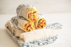 three burritos stacked on top of each other in a wrapper next to a tortilla