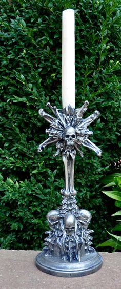 a silver candle holder sitting on top of a table next to some bushes and trees