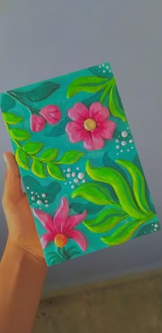 a hand holding up a painted square with flowers on the outside and green leaves on the inside