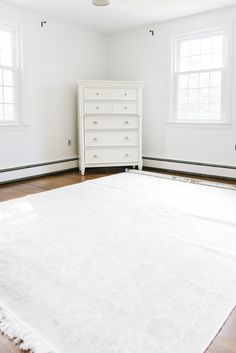 a white bed sitting in the middle of a room next to two windows and a dresser