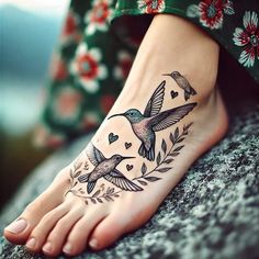 a woman's foot with a hummingbird and heart tattoo on the top of it