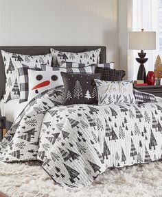 a bed covered in black and white comforter next to a night stand with two lamps