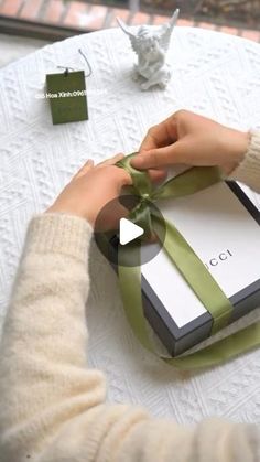 a woman is wrapping a gift box with a green ribbon on the table next to other items