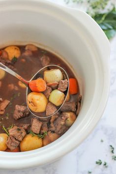 a ladle full of beef stew with potatoes and carrots