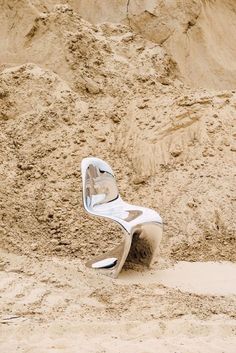 a white chair sitting on top of a sandy beach next to a hill covered in sand