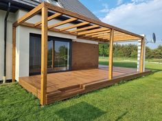 a wooden deck in front of a house with sliding glass doors on the side and an attached pergolated roof