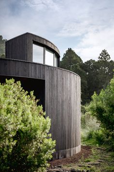 a round wooden structure in the middle of some bushes and trees, with windows on each side