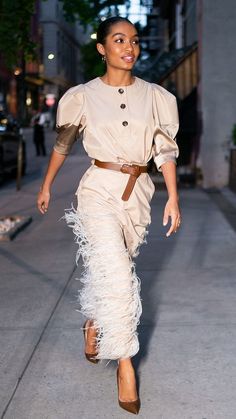 a woman is walking down the street in a feathery skirt and heels with her hand on her hip