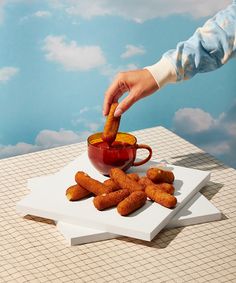 a person dipping something into a cup with sauce on it and some fried food in front of them