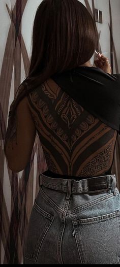 a woman with tattoos on her back standing in front of a wall