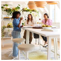 three women sitting at a table talking to each other in the middle of a room