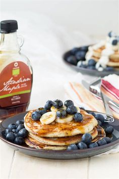 pancakes with blueberries and bananas on a plate next to maple syrup in a glass bottle