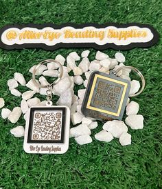 two keychains with qr code on them sitting in the grass next to some rocks