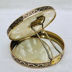 an open round metal box with a handle and gold trimmings on the lid