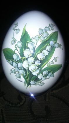 an egg with flowers painted on it sitting on a table next to a black background