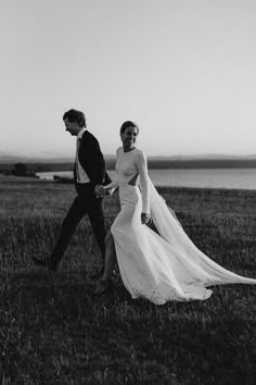 a bride and groom walking in the grass by the water on their wedding day, black and white photo