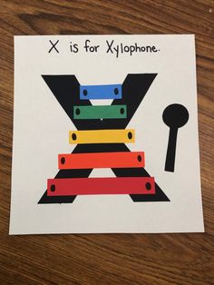 an x is for xylophone card with scissors and tape on it, sitting on a wooden table