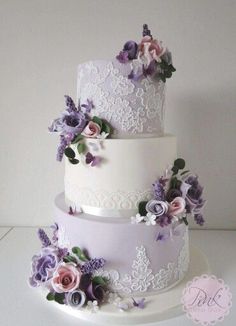 a three tiered wedding cake with purple flowers on the bottom and white frosting