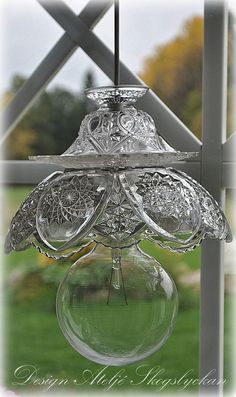 a glass hanging light fixture in front of a green lawn and fence with trees in the background