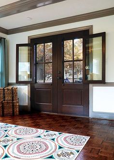 a large wooden door with two windows and a rug on the floor in front of it