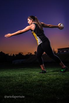 a woman is throwing a ball on the field at night with her arm extended out