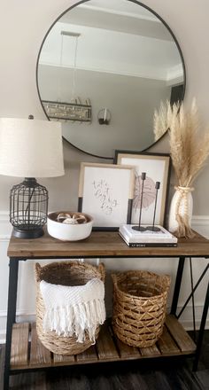 a wooden table topped with baskets next to a round mirror and framed pictures on the wall