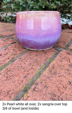 a pink and purple bowl sitting on top of a brick floor next to plants in the background