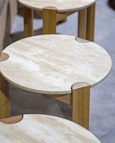 three round tables with wooden bases on display in a store or showroom, one is white marble and the other is brown wood