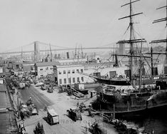 an old black and white photo of ships docked in the harbor with people walking around