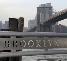 there is a sign that says brooklyn on it and the bridge in the back ground