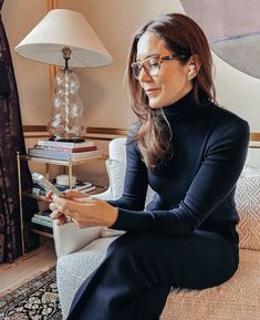 a woman sitting on a couch looking at her cell phone while wearing eyeglasses