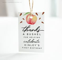 a thank card hanging from a string with an apple on it's tag that says, thanks a bushel for helping celebrate kinley's first birthday