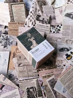 an open book sitting on top of a pile of newspaper paper covered in old advertisements