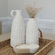 two white vases sitting on top of a wicker tray