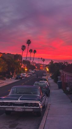 an old car is parked on the side of the road at sunset with palm trees in the background