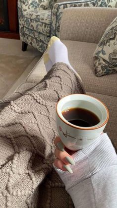 a woman holding a cup of coffee while sitting on a couch with her leg wrapped in a blanket