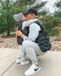 a woman kissing a man on the cheek while he is wearing a black jacket and grey sweatpants