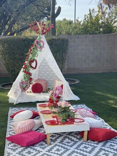 a teepee tent is set up in the grass with pillows and flowers on it