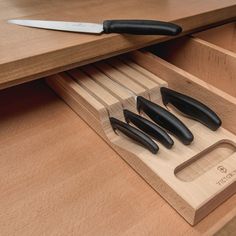 five knives in a wooden holder on top of a drawer with drawers underneath it and a knife sharpener next to them