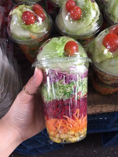 a person holding up a jar filled with salads and veggies in it