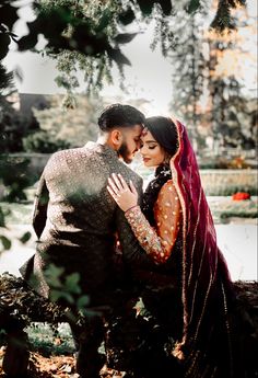 a man and woman are hugging in front of some trees with their arms around each other