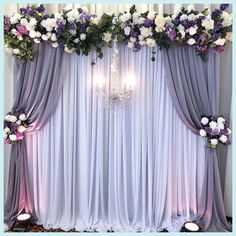 a purple and white wedding backdrop with flowers on the side, chandelier hanging from the ceiling