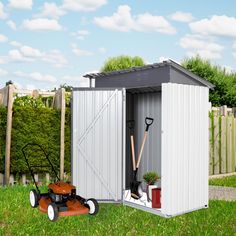 a garden shed with a lawn mower and gardening tools in the grass next to it