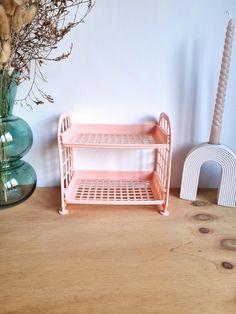 a pink shelf next to a vase with dried flowers in it on a wooden table