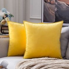 two yellow pillows sitting on top of a white couch next to a vase with flowers