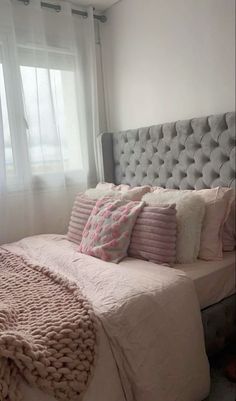 a bed with pink and white pillows in a bedroom next to a curtained window