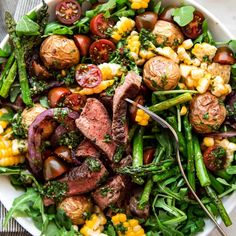 a salad with steak, corn and tomatoes in a white bowl on top of a table