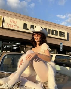 a woman sitting on the hood of a car in front of a liquor store with her legs crossed