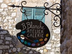 a black sign hanging from the side of a stone building next to a blue window